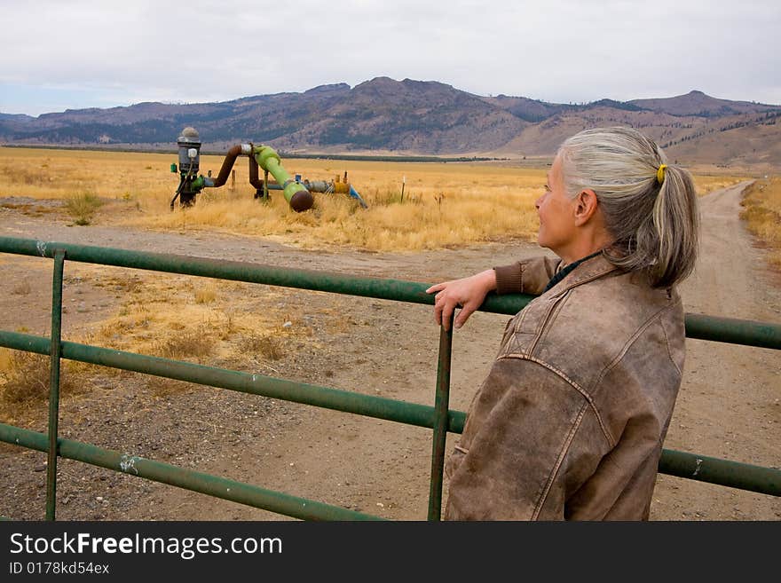 Mature female rancher standing at gate to ranch for last time.