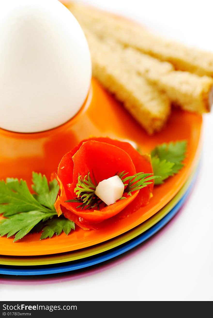 Boiled white egg in a colorful holder decorated with bread and tomato flower as decoration - closeup. Boiled white egg in a colorful holder decorated with bread and tomato flower as decoration - closeup