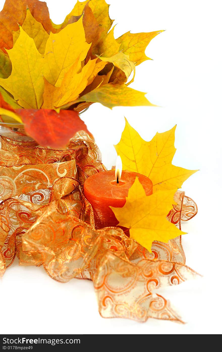 Bright maple leafs arranged in a glass vase with ribbon and lighted candle - closeup. Bright maple leafs arranged in a glass vase with ribbon and lighted candle - closeup