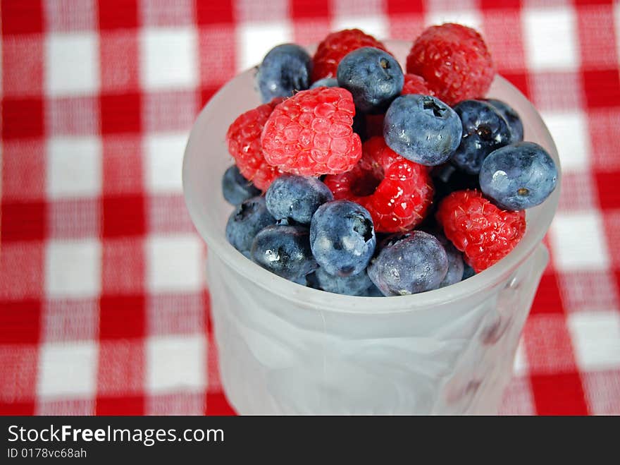 Fresh blueberries and raspberries in a goblet on checkered fabric. Fresh blueberries and raspberries in a goblet on checkered fabric.