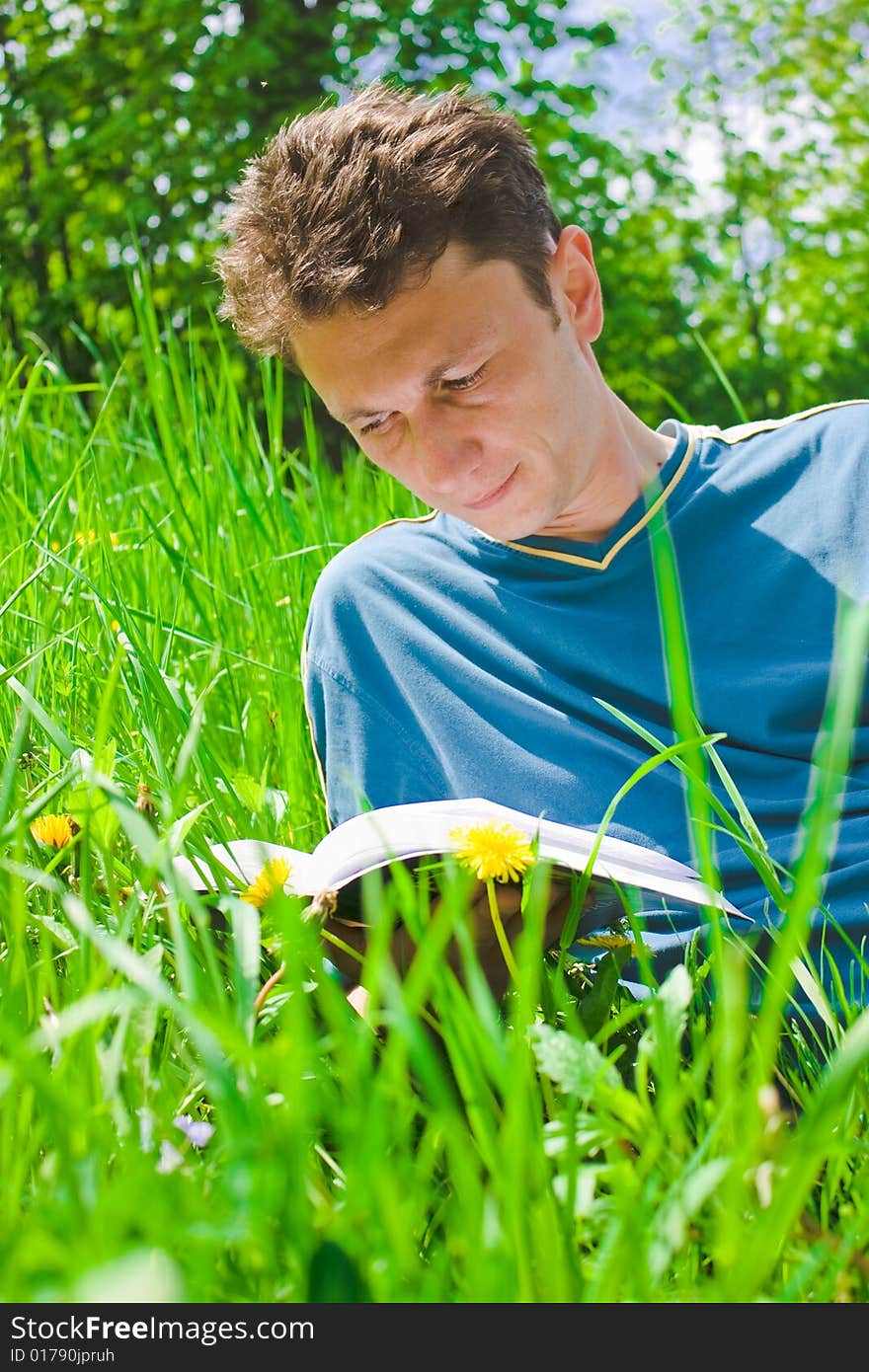 Portrait of a young man reading in grass