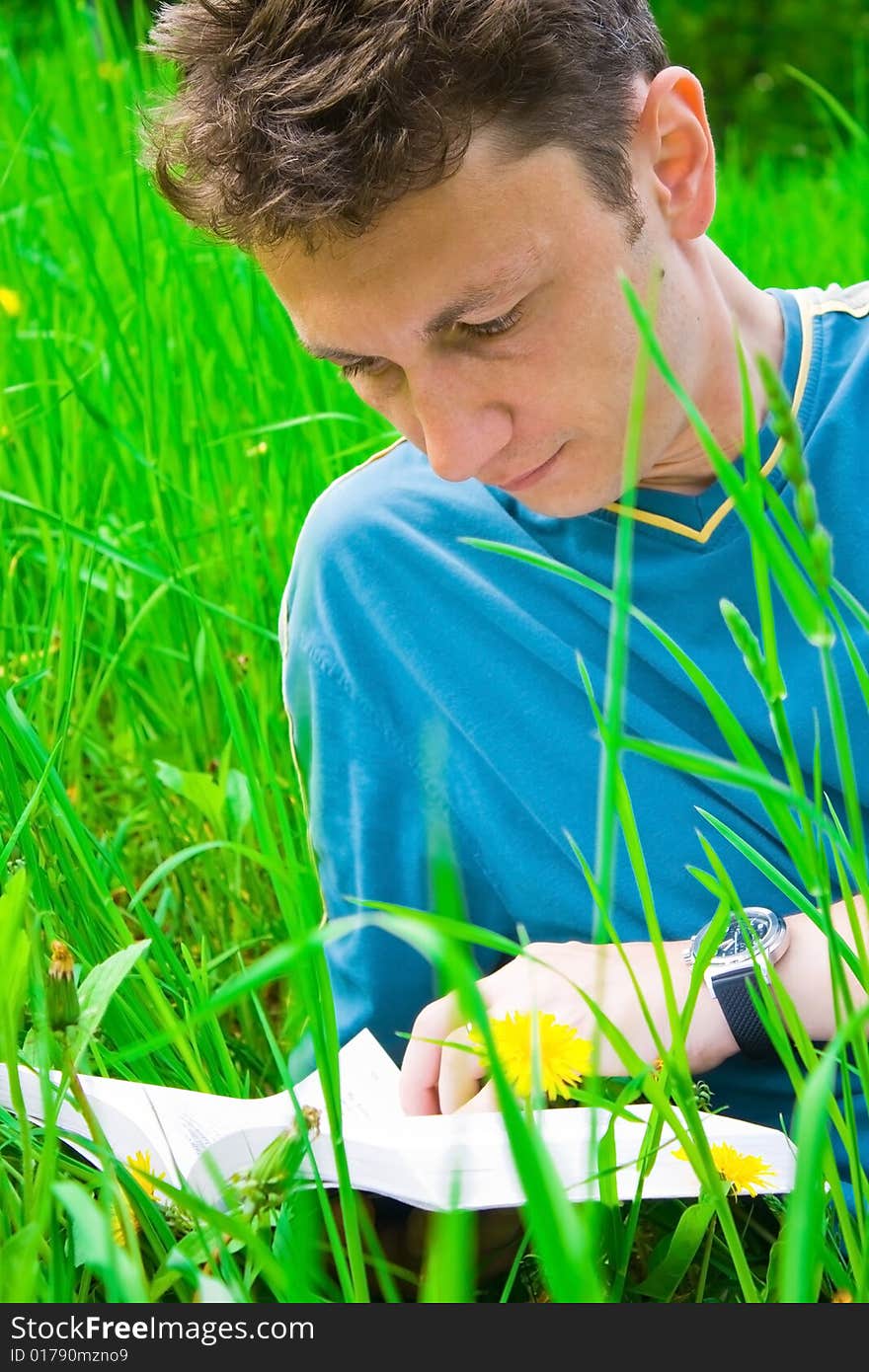 Portrait of a young man reading in grass