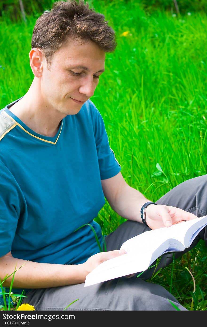 Portrait of a young man reading in grass