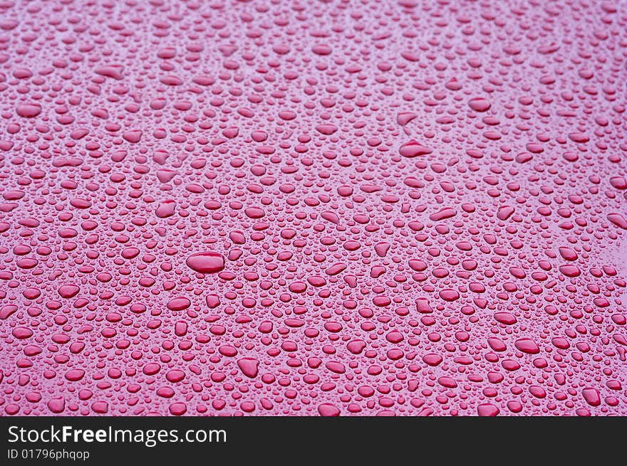 A picture of water drops on a red metal surface. A picture of water drops on a red metal surface