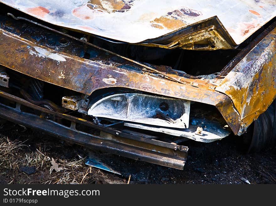 A close up of the front of a burned out car abandoned in a field. A close up of the front of a burned out car abandoned in a field.