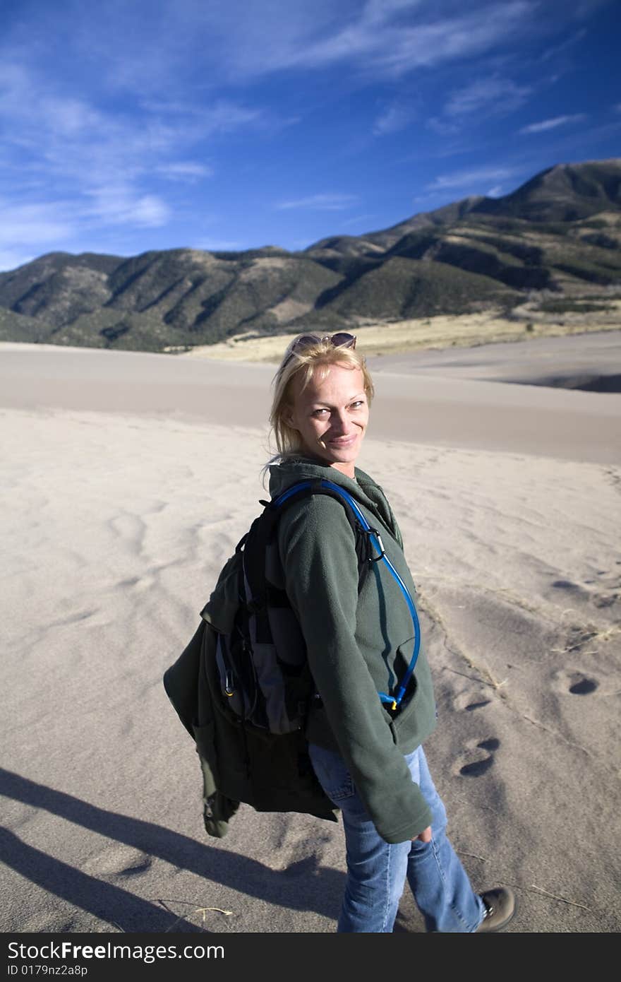 An adult woman smiling as she looks over her shoulder during a hike. Looking back the direction she has traveled in the setting sun, she shows enjoyment or happiness on her face. Great Sand Dunes National Park, Colorado. An adult woman smiling as she looks over her shoulder during a hike. Looking back the direction she has traveled in the setting sun, she shows enjoyment or happiness on her face. Great Sand Dunes National Park, Colorado