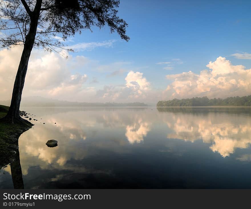 Stratocumulus clouds in a clear blue sky in the morning seen at the edge of a still lake. Stratocumulus clouds in a clear blue sky in the morning seen at the edge of a still lake