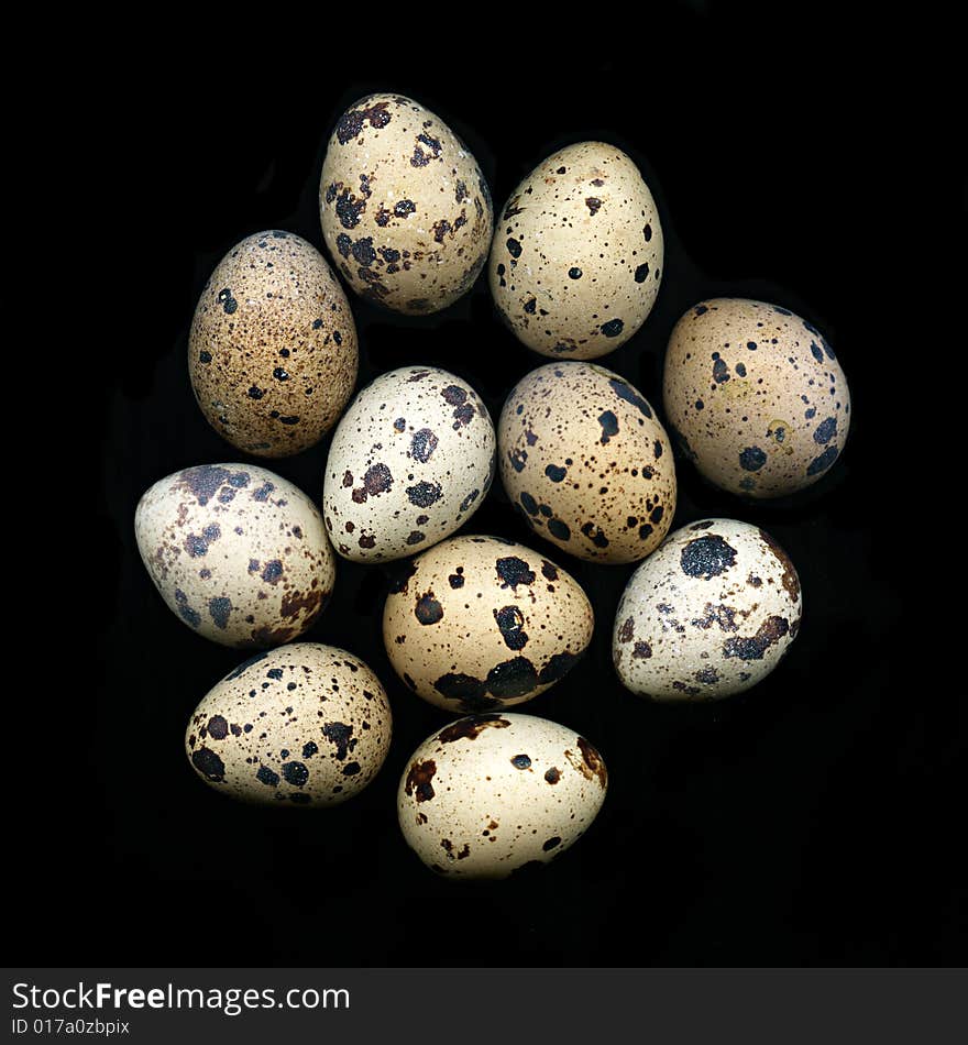 A pile of quail eggs against black background