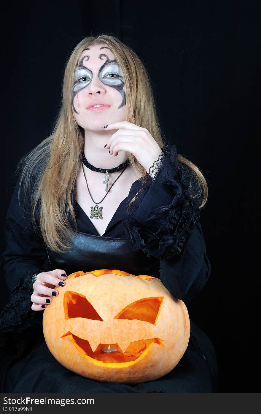 Portrait of pretty vampire girl with halloween pumpkin on black background