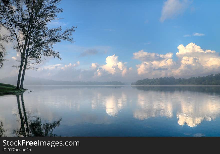 Stratocumulus clouds in a clear blue sky in the morning seen at the edge of a still lake. Stratocumulus clouds in a clear blue sky in the morning seen at the edge of a still lake