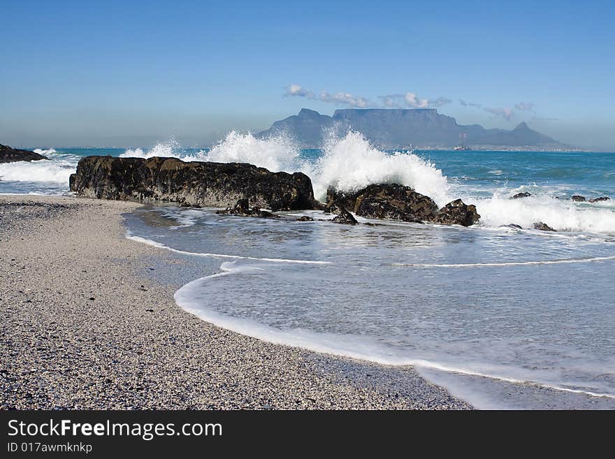 Table Mountain from Bloubergstrand with rocks in the foreground and water splash