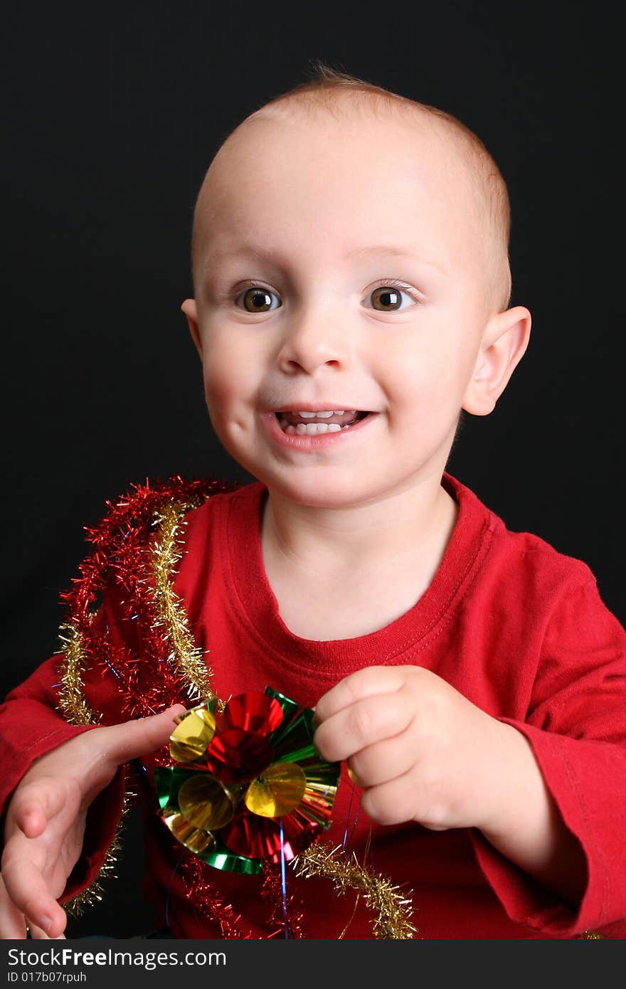 Toddler against a black background playing with christmas decorations