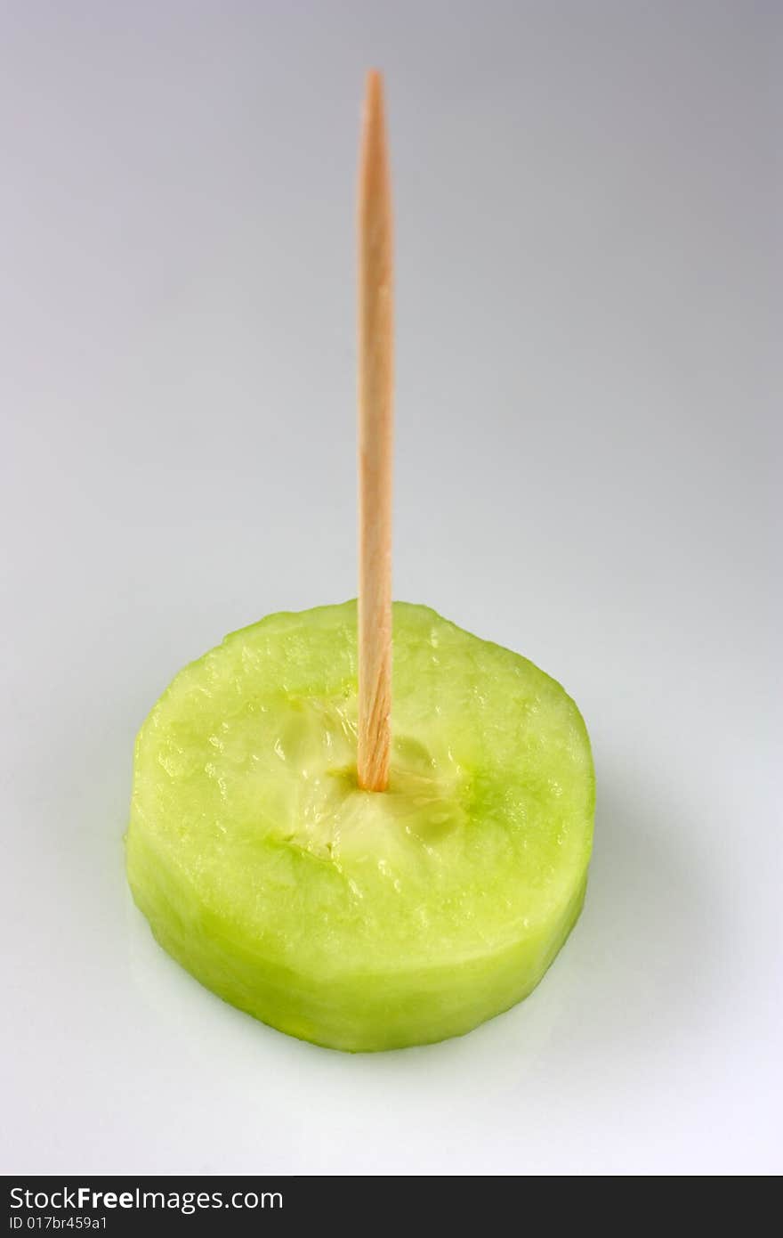 A slice of cucumber served with a toothpick on it. A slice of cucumber served with a toothpick on it