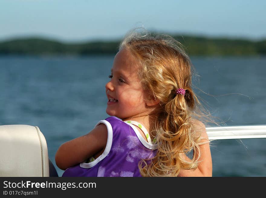 A three year-old girl – wearing her lifejacket – smiles back at one of her parents while riding on a boat out on a lake on a sunny afternoon. A three year-old girl – wearing her lifejacket – smiles back at one of her parents while riding on a boat out on a lake on a sunny afternoon.