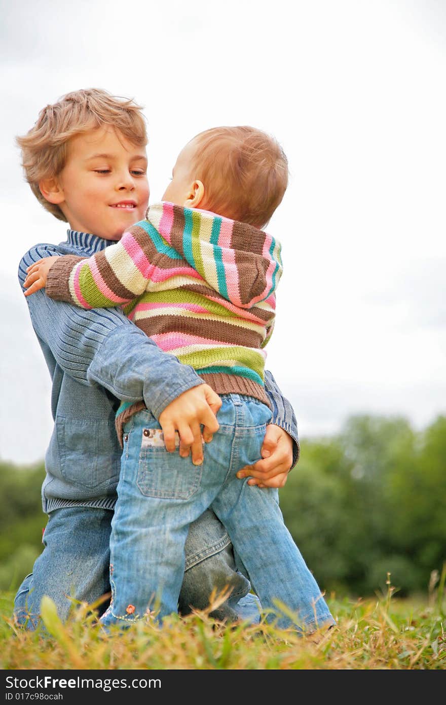 Boy embraces child on green grass. Boy embraces child on green grass