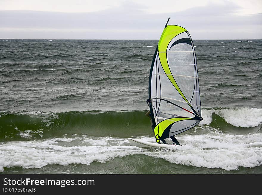 Windsurfer gliding on waves in overcast day. Windsurfer gliding on waves in overcast day