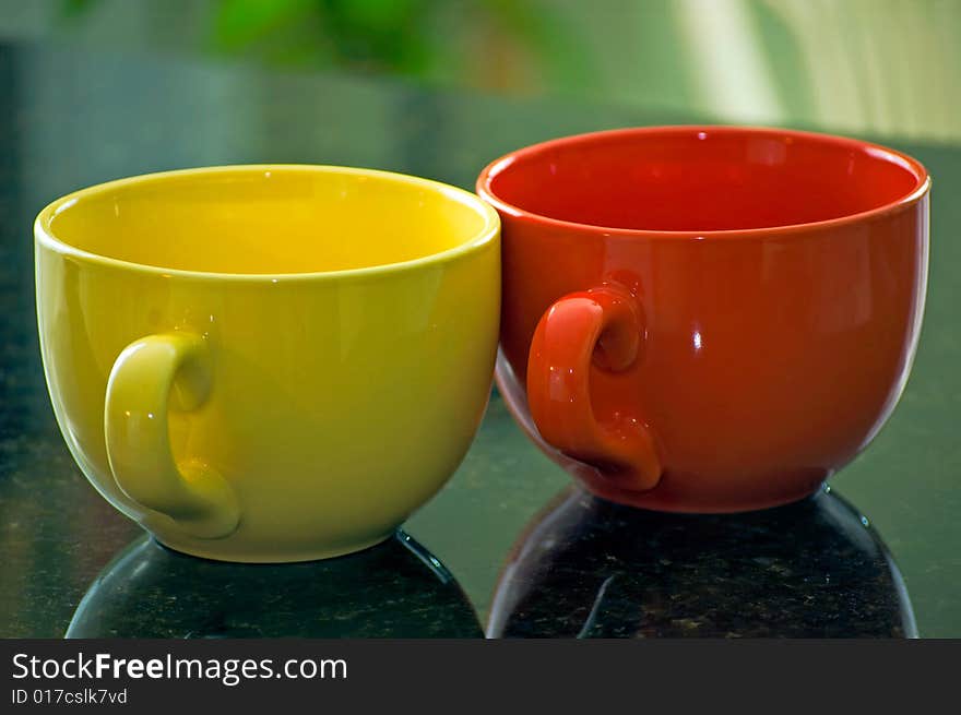 A yellow and orange coffee mug sit on a marble countertop. A yellow and orange coffee mug sit on a marble countertop