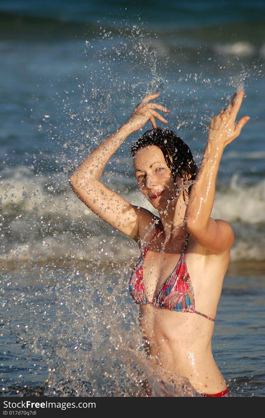 A young woman splashes in the shallows at the beach. A young woman splashes in the shallows at the beach