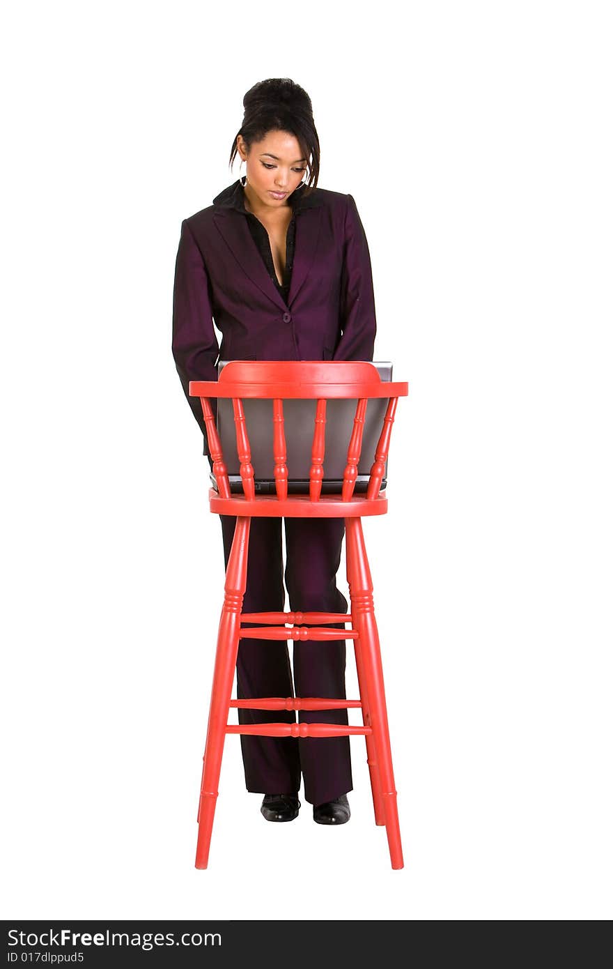 Young businesswoman using a laptop on a red stall. Model is looking down at the laptop. Young businesswoman using a laptop on a red stall. Model is looking down at the laptop