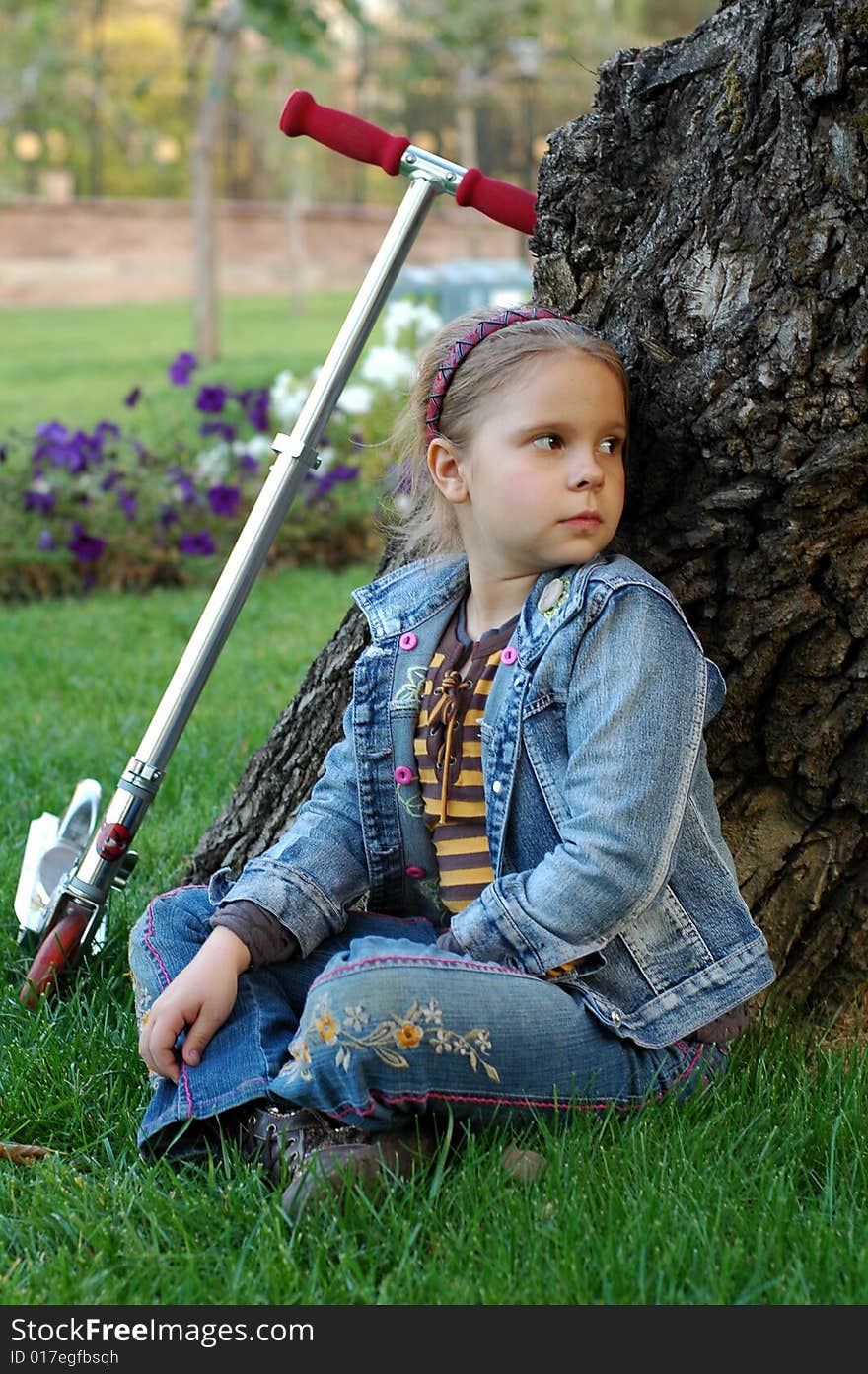 Little girl with scooter sitting under the tree