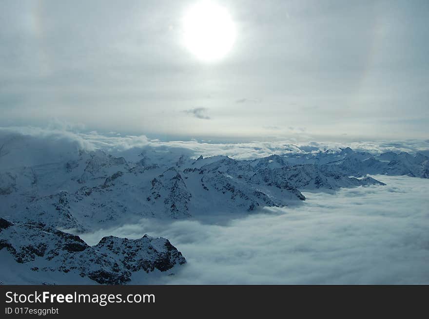 Huge mountains broken up by a tide of cloud winding through it, stretching into the distance. The sun casts a glow over the scene. Huge mountains broken up by a tide of cloud winding through it, stretching into the distance. The sun casts a glow over the scene.