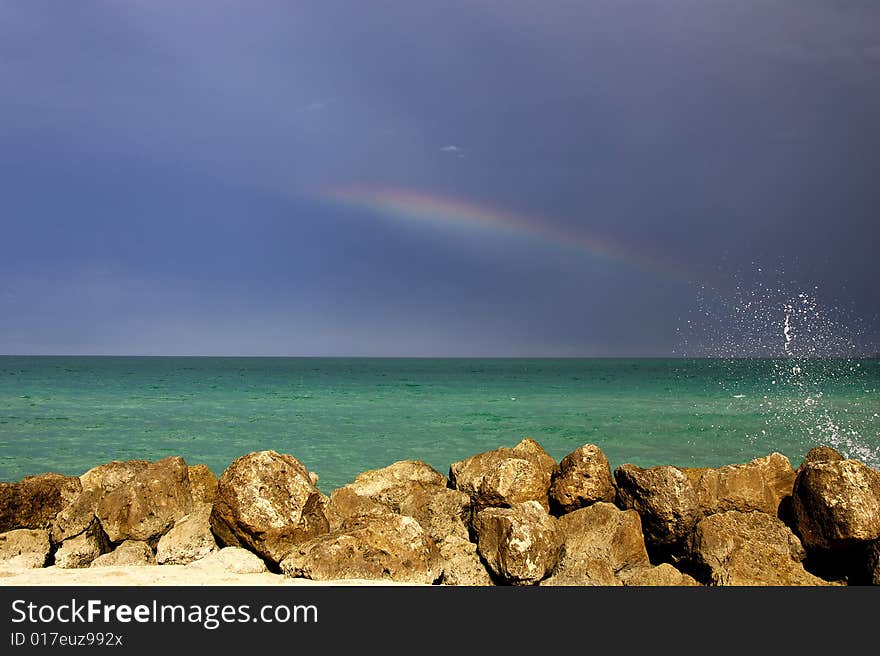 Little rainbow above ocean, blue sky and clounds