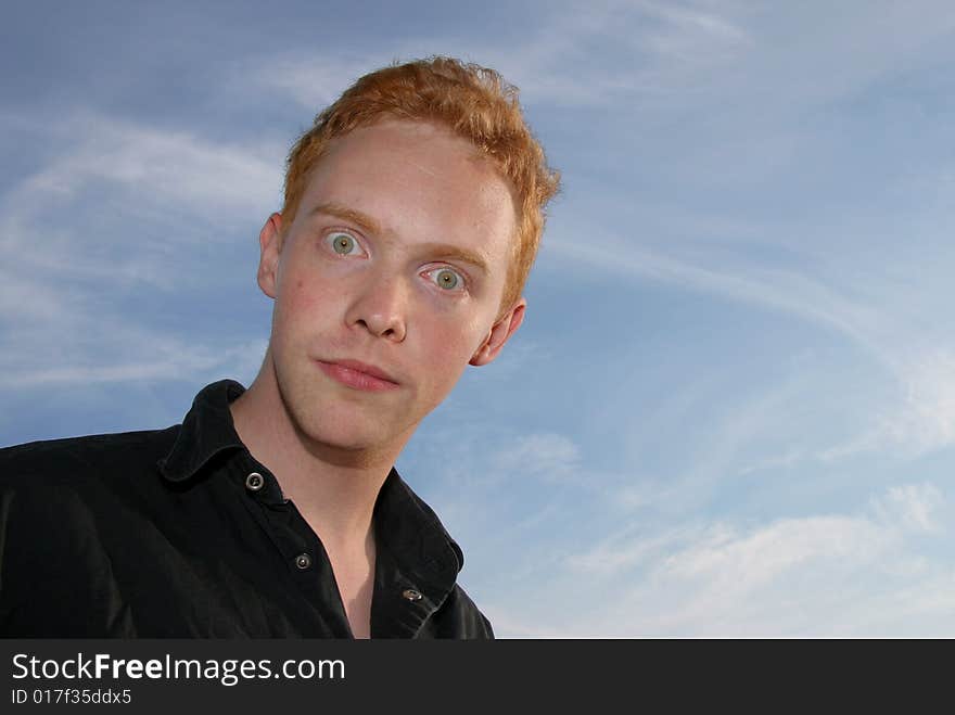 A bizarre young man staring wide-eyed against blue sky. A bizarre young man staring wide-eyed against blue sky.