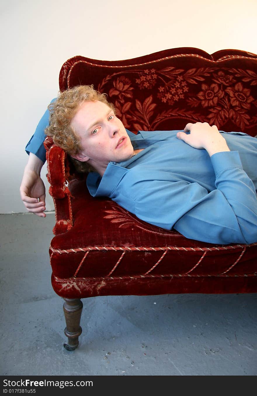 A young red-haired man lying on an old red sofa. A young red-haired man lying on an old red sofa.