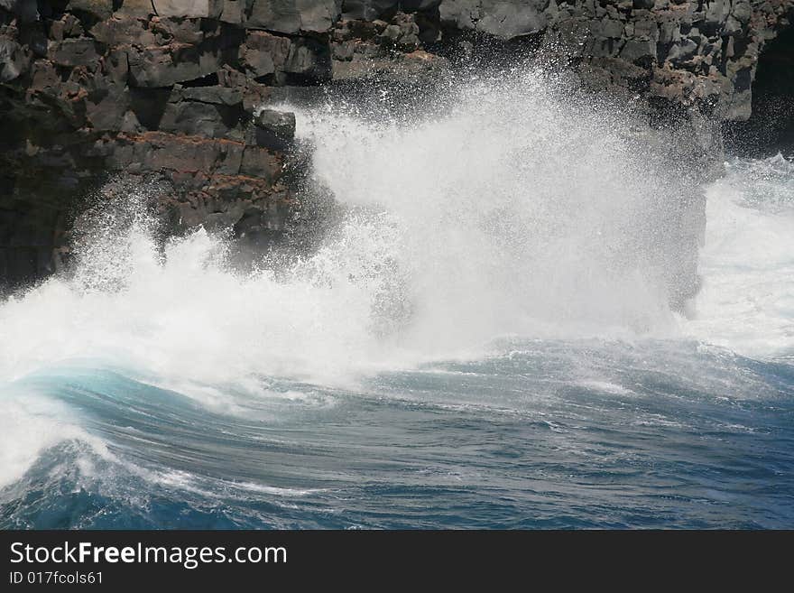 A hard blue wave crashes against a cliff on the coast. A hard blue wave crashes against a cliff on the coast