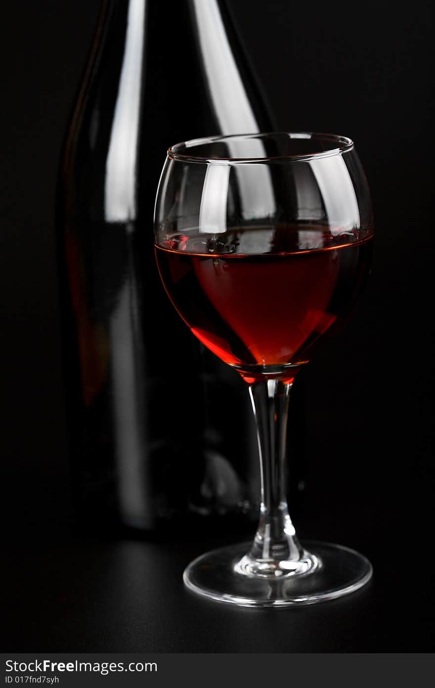 Glass of red wine and bottle over black background