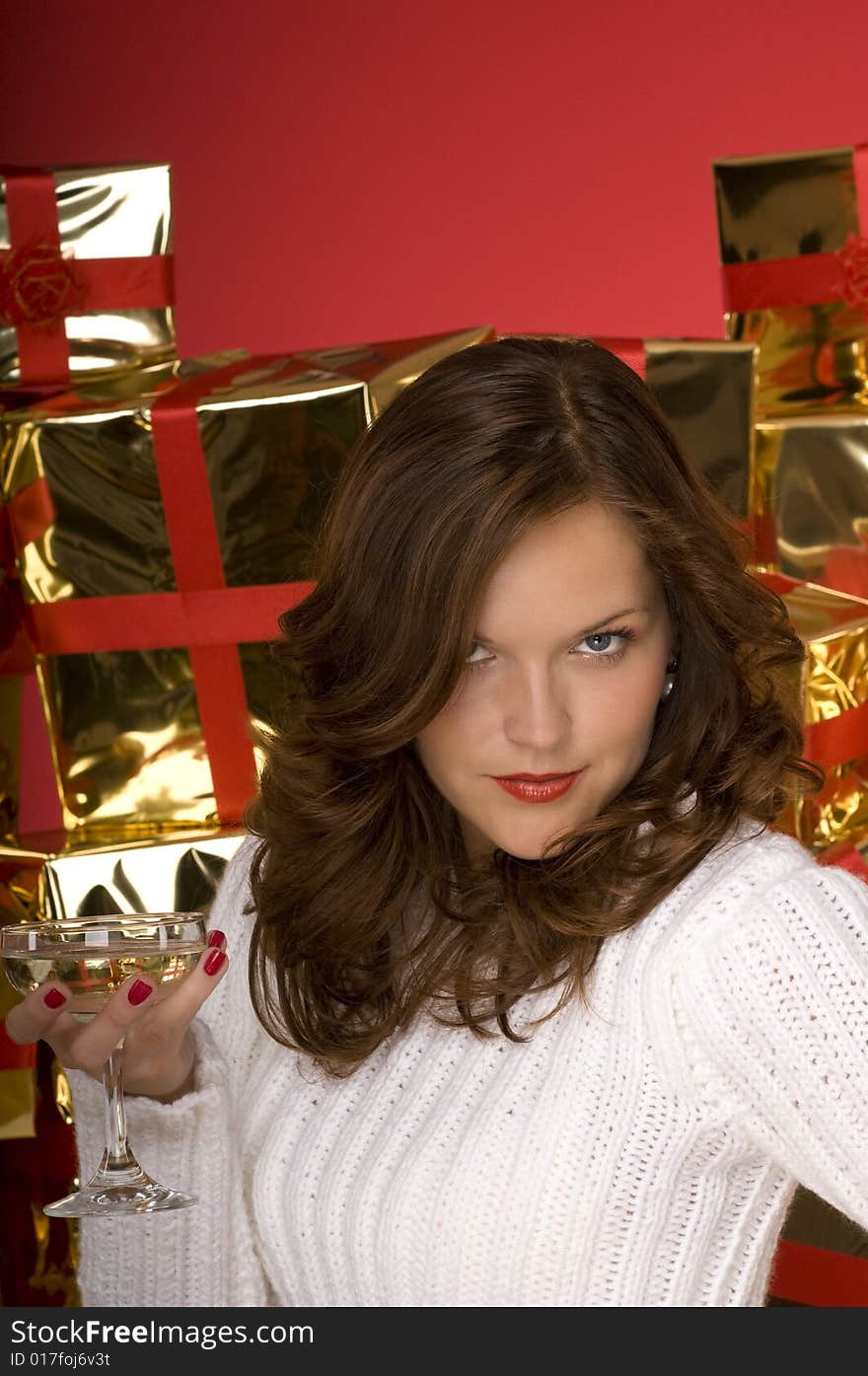 Provocative beautiful woman with champagne coupe in front of golden wrapped Christmas presents