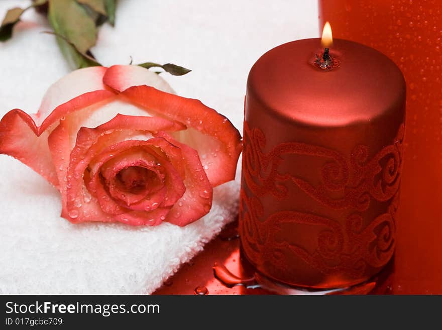 Candle with rose and towel on red background