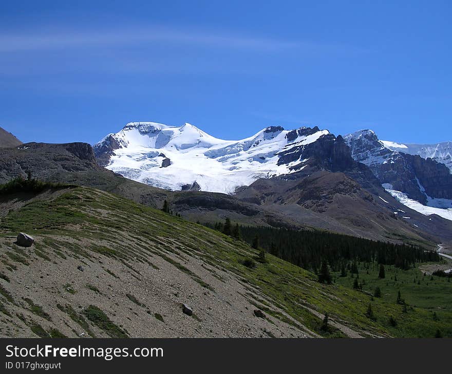 A snow covered Canadian mountain framed by meadows and a gravelly slope.