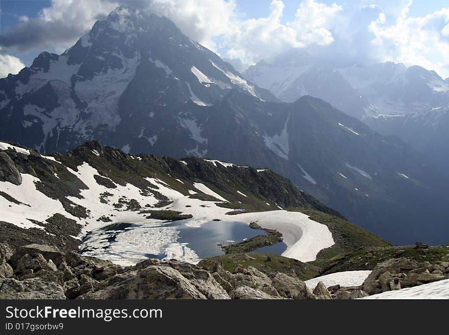 Mountain lake at Caucasus, half-covered by ice. Mountain chain on background. ~9000 ft over the sea level. July 2007.