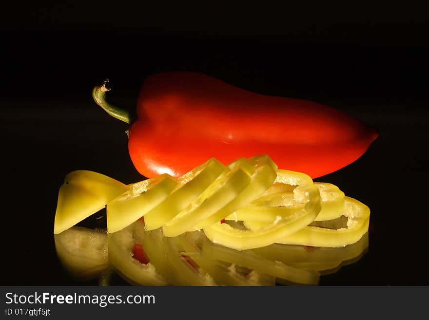 Red and slit green pepper with reverberation lying on black background. Red and slit green pepper with reverberation lying on black background