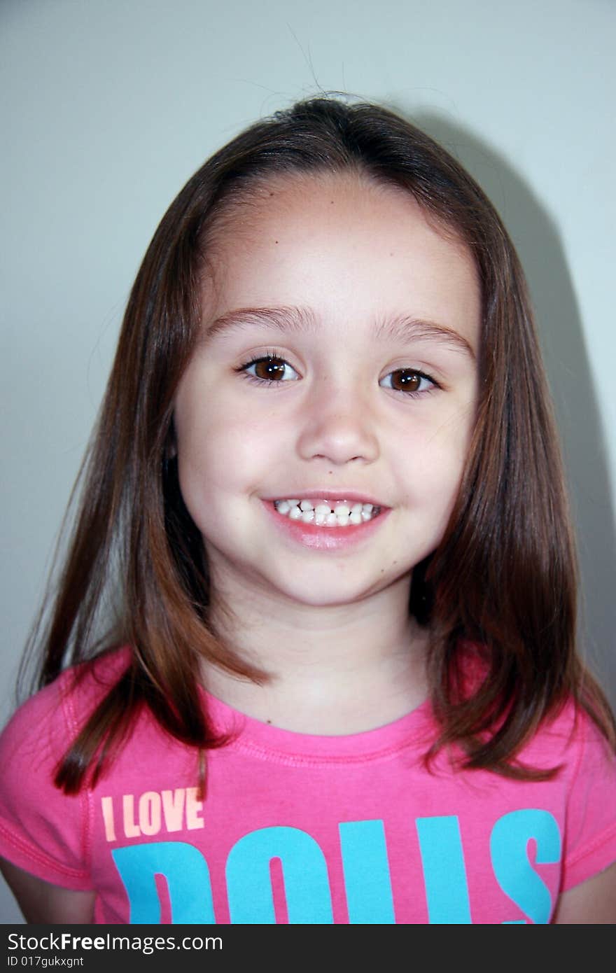 Portrait of a smiling 4 year old caucasion female child, with shoulder length straight brown hair, and a pink collarless tshirt displaying the motiff -'I love dolls'. Portrait of a smiling 4 year old caucasion female child, with shoulder length straight brown hair, and a pink collarless tshirt displaying the motiff -'I love dolls'.