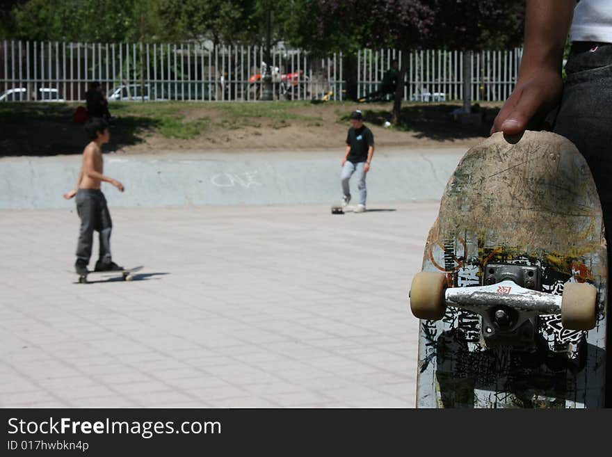 A kid showing his skate board with another skaters on the background