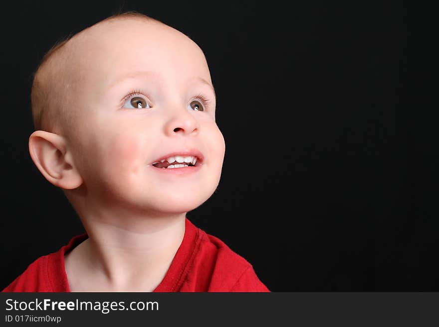 Blonde toddler against a black background looking up