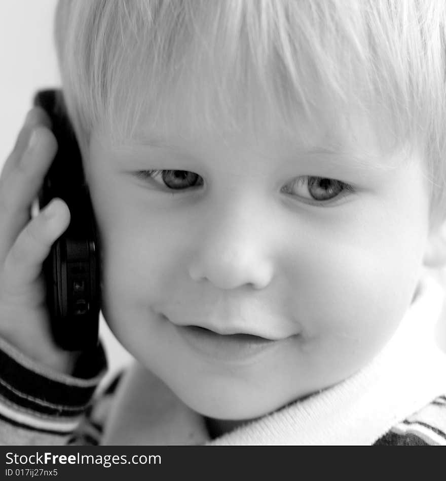 The child smiles and speaks on the phone. The child smiles and speaks on the phone