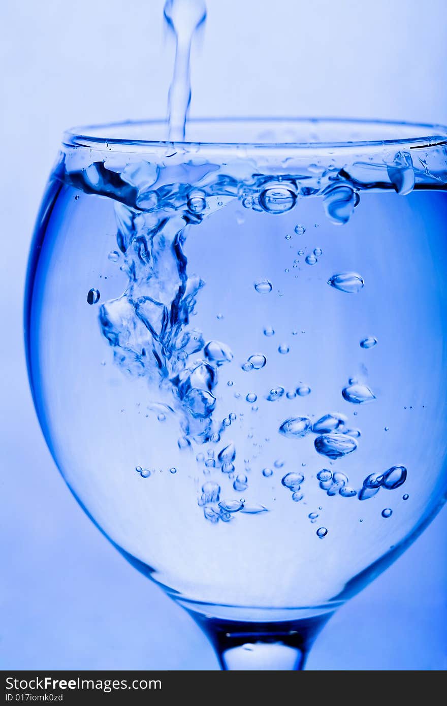 Water pouring into glass toned blue