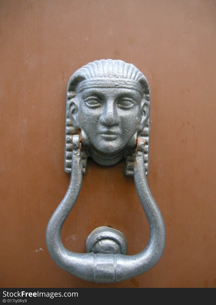 A silver door knocker in Egyptian style on brown background. A silver door knocker in Egyptian style on brown background