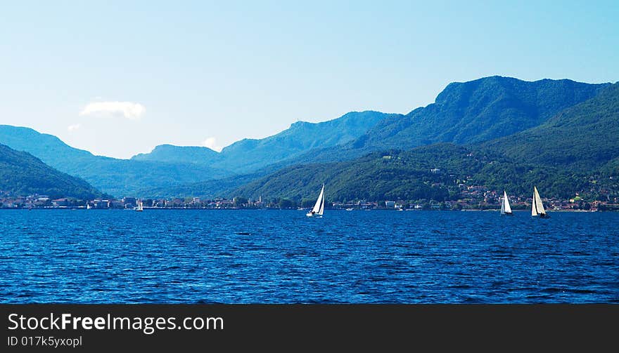 A blue lake with white boats sailing. The name is 'Maggiore lake', Italy. Blue and green tones. A blue lake with white boats sailing. The name is 'Maggiore lake', Italy. Blue and green tones.