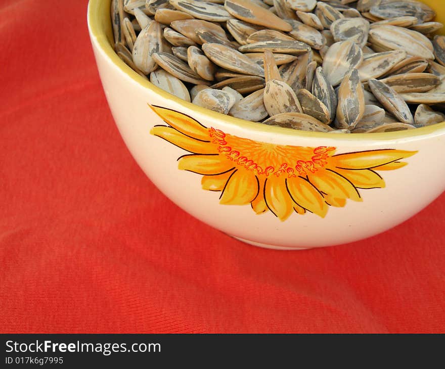 Sunflower seeds in a bowl with a sunflower decoration on red background