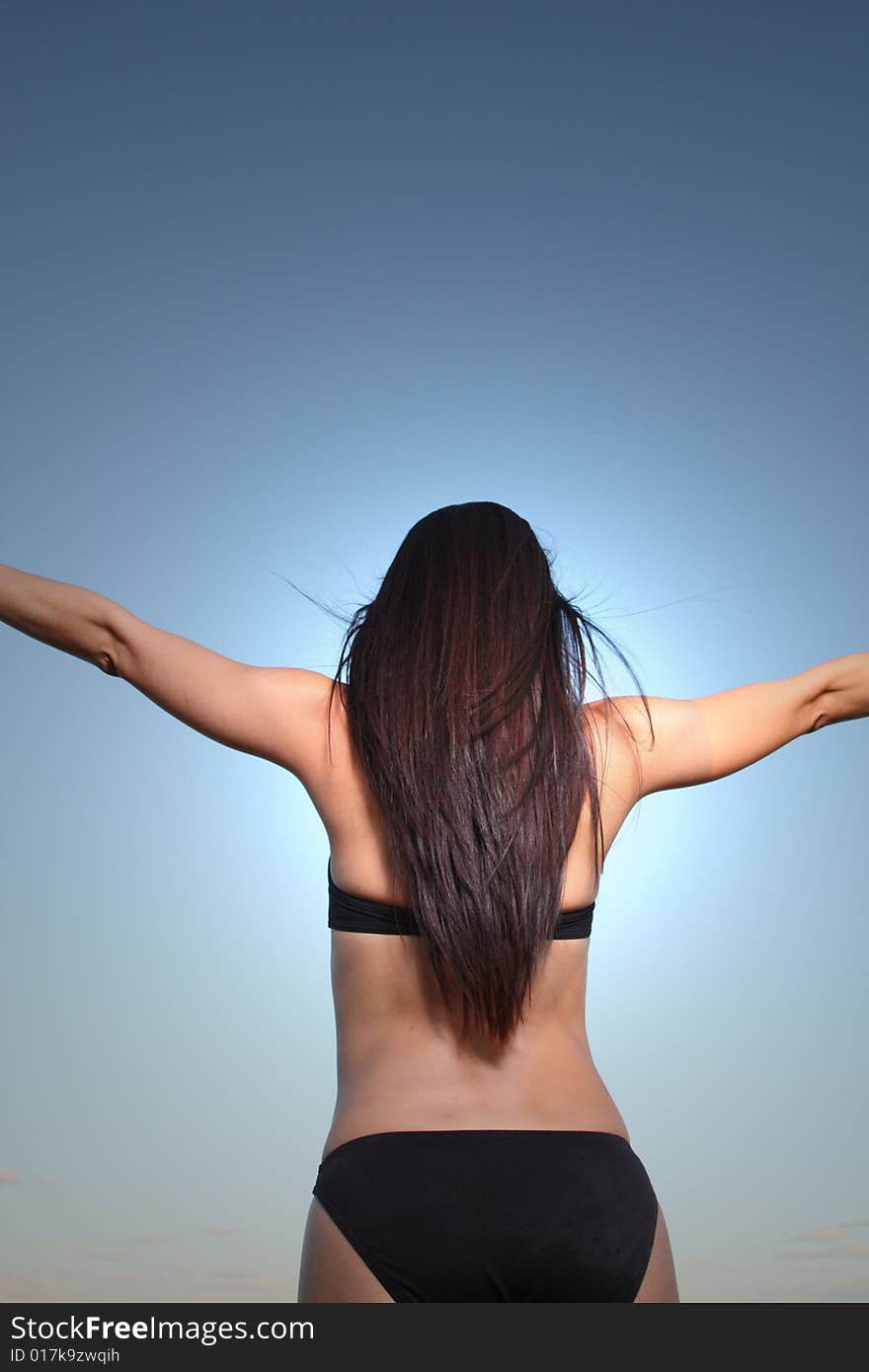 Young female in a bikini facing away towards the sky. Young female in a bikini facing away towards the sky.