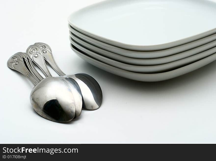 Pile of white plates and shining spoons on a white background. Preparation for table layout.