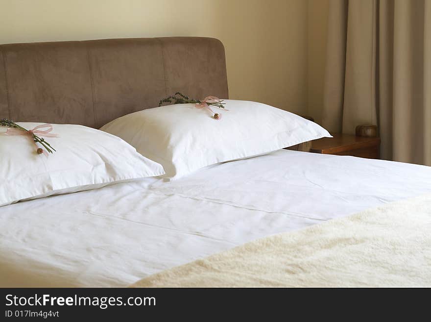 Beautiful bedroom interior with white sheets and flower decorations on pillows. Warm tone