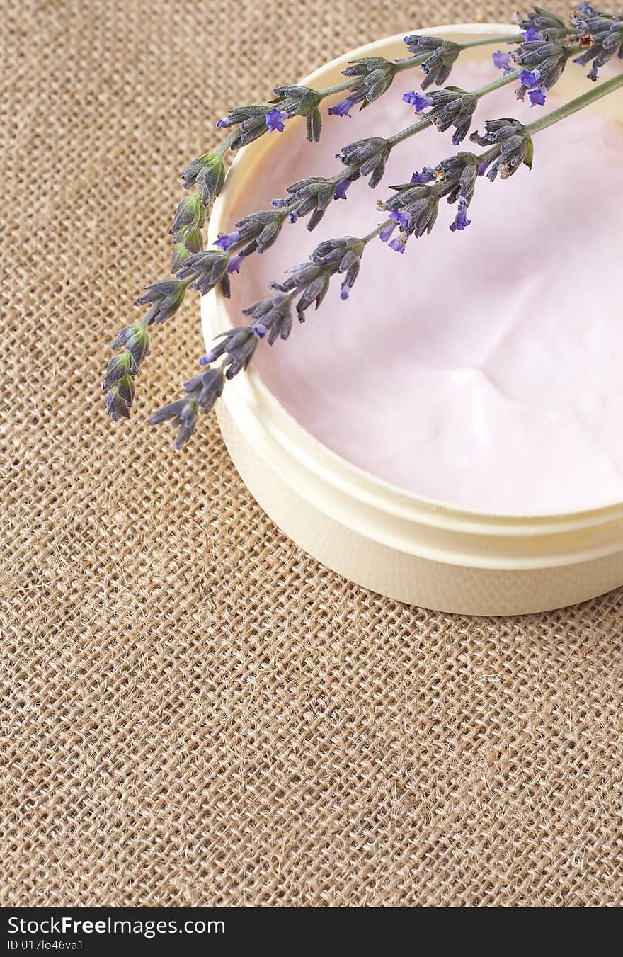 Relaxing spa scene with pink body butter in a jar and some lavender stems on mesh material bacground with copy space