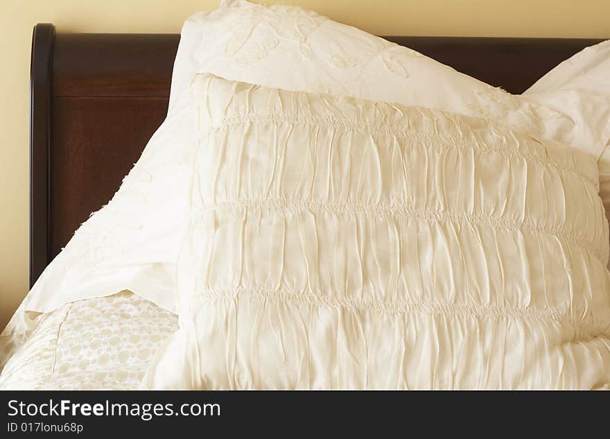 Beautiful bedroom interior with ivory color decorative cushions and wooden bedpost. Warm tone