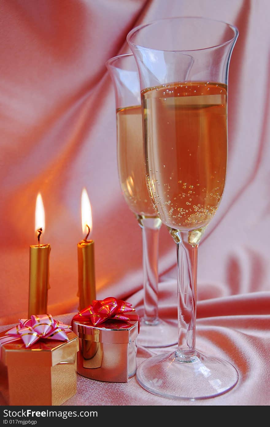 Pair of champagne flutes with candles and gift box on silk background