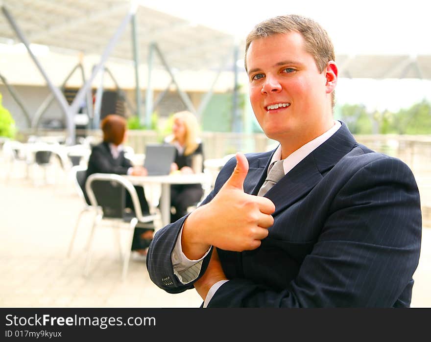 Business man giving ok sign or thumb up with happy expression. two other business women on the background. Business man giving ok sign or thumb up with happy expression. two other business women on the background